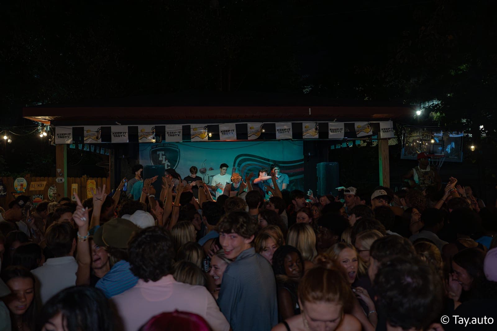 Outdoor stage, crowd hands up under string lights and trees