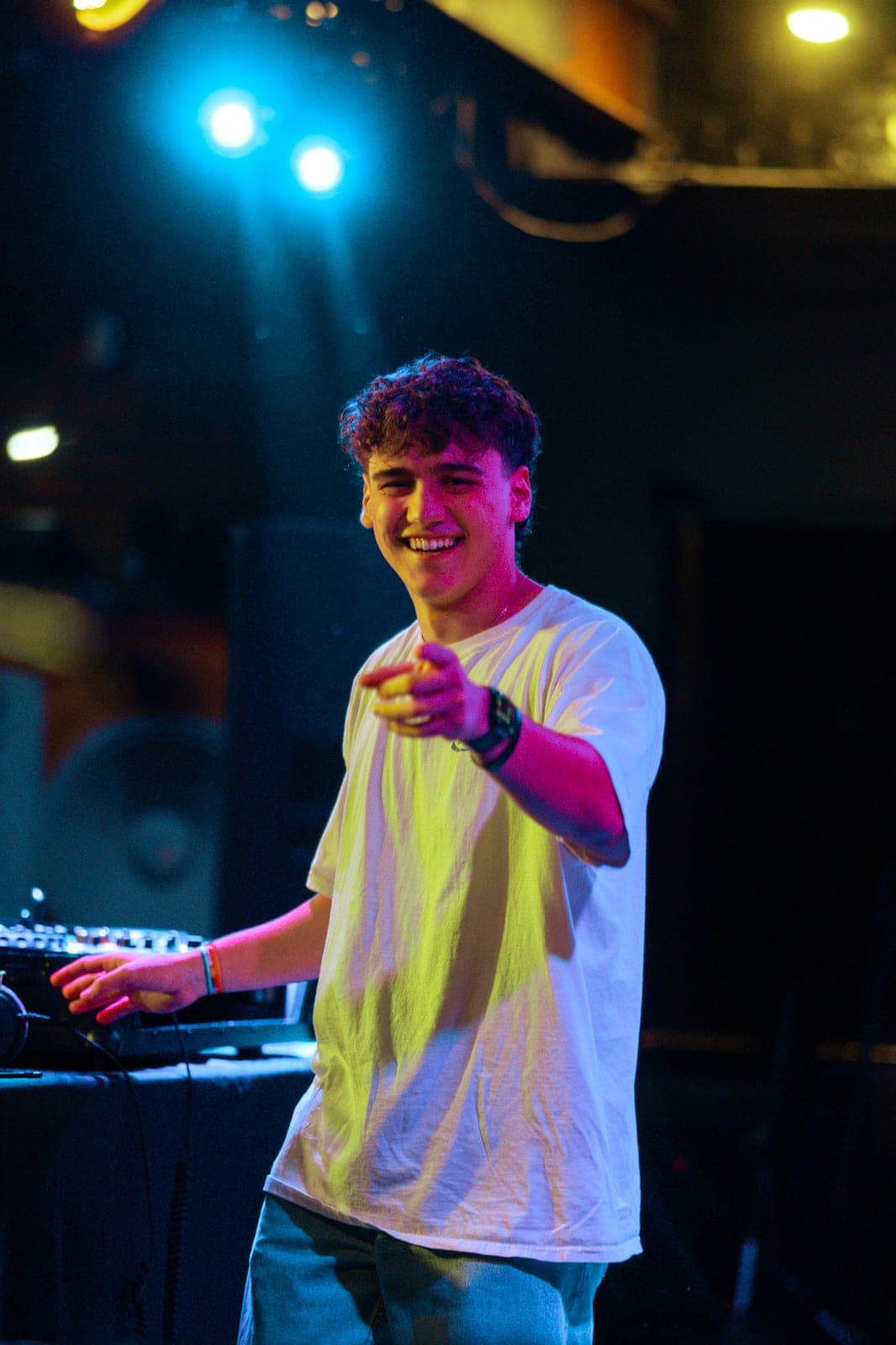 Portrait, smiling and pointing at the camera under blue and yellow club lighting