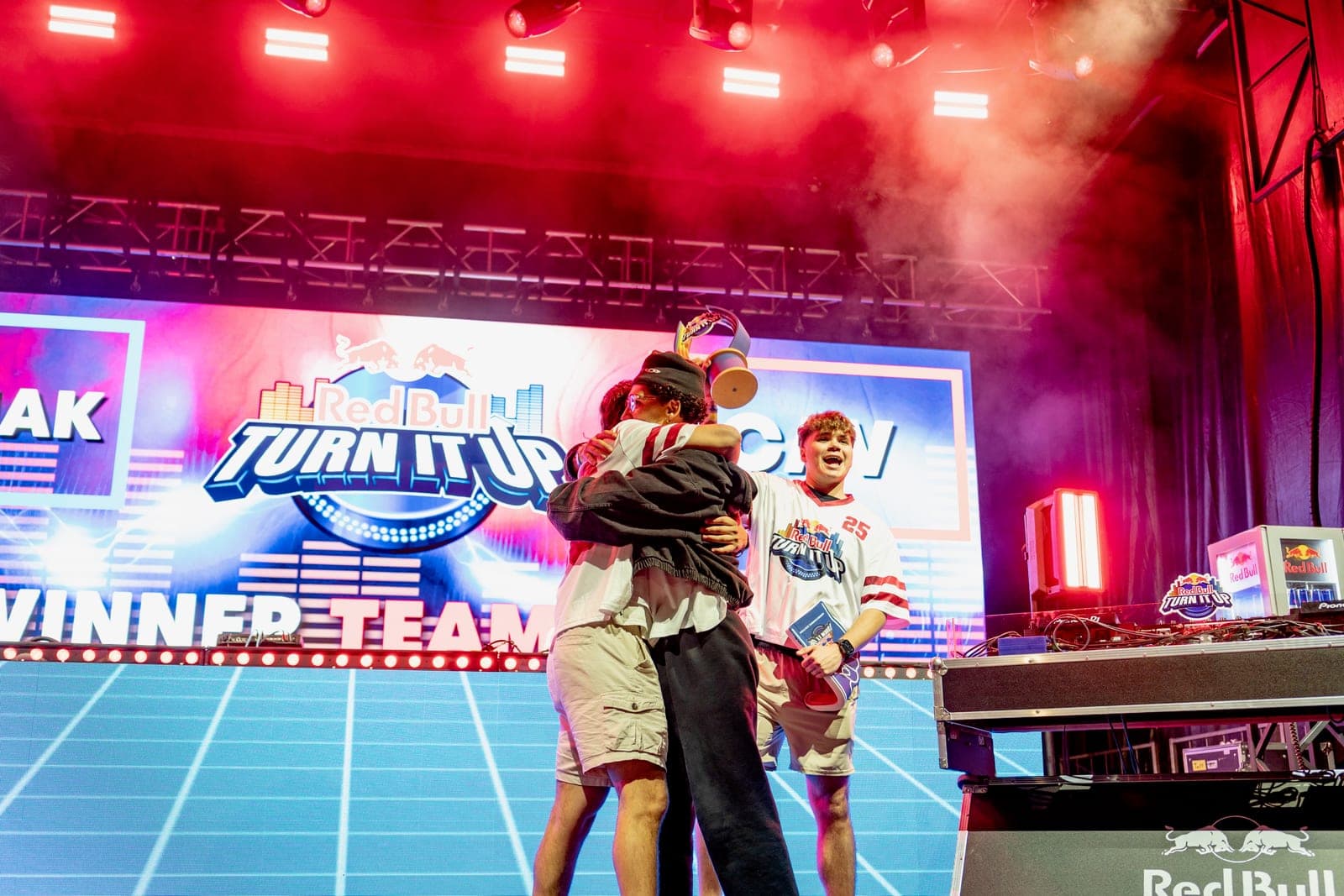 CAV hugging a teammate onstage, Red Bull Turn It Up winner banner behind them